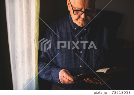 Elderly man stand next to window and reading Bible Elderly man stand next to window and reading Bible 78218053