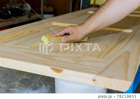 Carpenter in work on worker sanding with sanding block wooden door 78219655