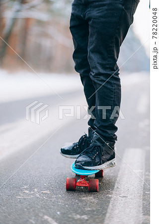 Skateboarder standing on the road in the middle of the forest, surrounded by snow 78220048