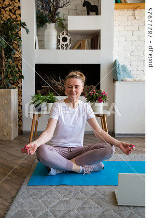 Portrait of young woman doing yoga online sitting in lotus position on yoga mat Portrait of young woman doing yoga online sitting in lotus position on yoga mat 78222925