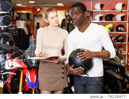 Polite smiling female seller communicating with male customer in modern motorcycle salon Polite smiling female seller communicating with male customer in modern motorcycle salon 78226977