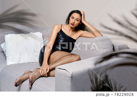 Barefoot african american woman sits with legs tucked on couch 78229028