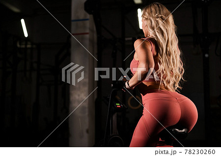 Unrecognizable blonde with elastic buttocks is training in an air bike. Athletic woman is engaged in the gym on an exercise bike. Unrecognizable blonde with elastic buttocks is training in an air bike. Athletic woman is engaged in the gym on an exercise bike. 78230260