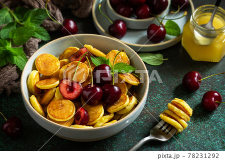 Trendy home breakfast. Mini pancakes, honey and cherries on a stone table. Trendy home breakfast. Mini pancakes, honey and cherries on a stone table. 78231292