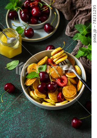 Trendy home breakfast. Mini pancakes, honey and cherries on a stone table. Copy space. 78231295