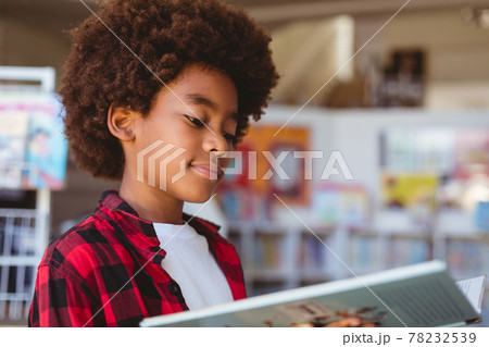 Smiling african american schoolboy reading book standing in school library 78232539