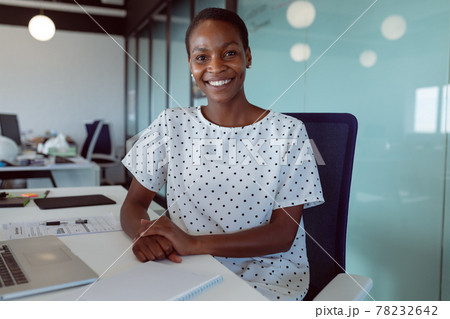 Smiling african american businesswoman sitting at desk at work Smiling african american businesswoman sitting at desk at work 78232642