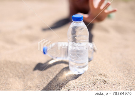Man reaches for bottle of water standing on sand Man reaches for bottle of water standing on sand 78234970