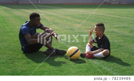 Diverse trainer and boy talking on football pitch 78239489