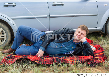 The tired driver lies on a blanket near the car The tired driver lies on a blanket near the car 78246423