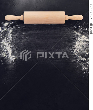Wooden rolling pin in hands and flour. Bakery on a black stone background. 78249963