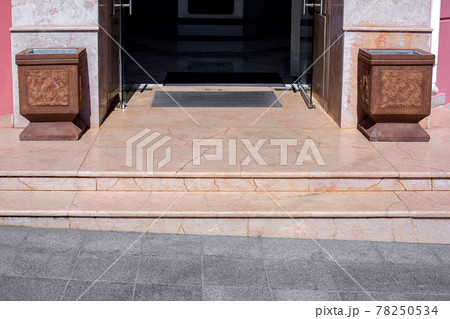 granite threshold with steps at the entrance to the store with a foot mat and stone trash can pots at the facade of the building close-up front view, nobody. 78250534