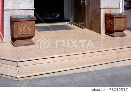 granite threshold with steps at entrance to store with foot mat and stone trash can pots at facade of european style architecture building close-up view on sunny day, nobody. 78250537