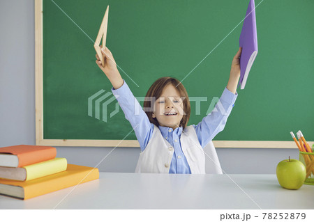 Schoolboy sitting at desk in classroom and holding up notebook with ruler. Back school concept. 78252879