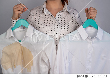 A woman compares two white shirts before and after washing. The girl is holding one blouse, clean and ironed, and the other, dirty with coffee stains 78253071