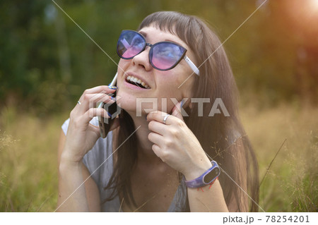 young woman emotionally speaks on the phone on the lawn on a sunny day. happy emotion on the face. 78254201