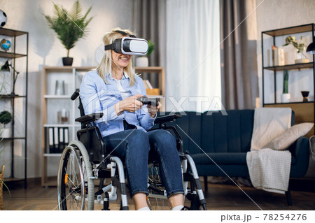 Woman in wheelchair playing virtual games in 3D glasses Woman in wheelchair playing virtual games in 3D glasses 78254276