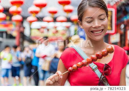Chinese woman eating Bing Tang Hulu, a traditional chinese food snack from Beijing. Fruit candy stick sold in outdoor market place on Wangfujing street. Candied fruits on a bamboo stick Chinese woman eating Bing Tang Hulu, a traditional chinese food snack from Beijing. Fruit candy stick sold in outdoor market place on Wangfujing street. Candied fruits on a bamboo stick 78254323