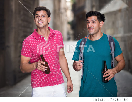 Two male friends are walking and drinking beer 78263166