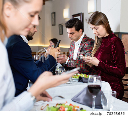 Modern young people busying with phone during evening meal at restaurant Modern young people busying with phone during evening meal at restaurant 78263686