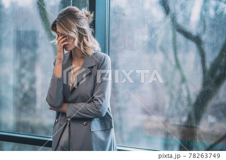 Woman covering her face with hand near window 78263749