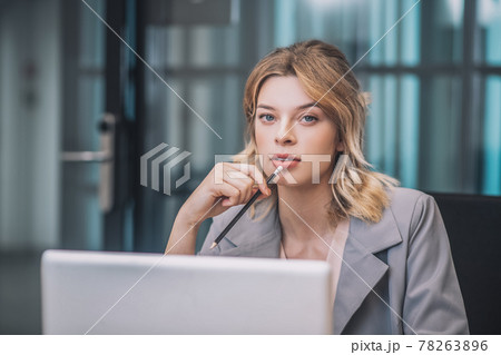 Meditative woman with pencil at laptop 78263896