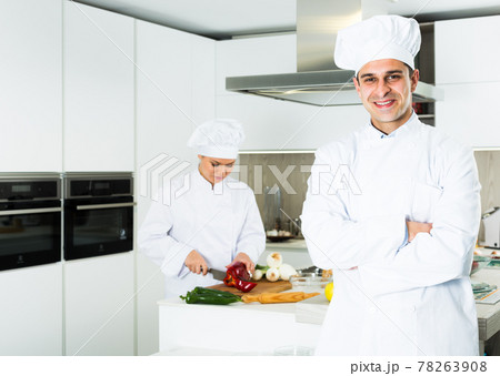 Smiling male kitchener in uniform is standing in the kitchen Smiling male kitchener in uniform is standing in the kitchen 78263908