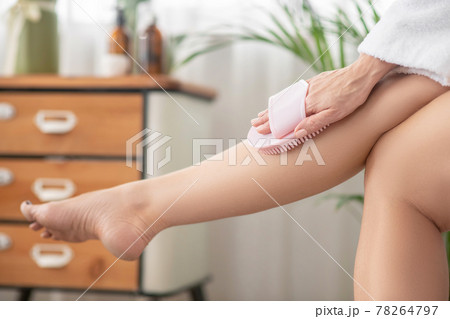 Woman in white massaging her legs with massaging device Woman in white massaging her legs with massaging device 78264797