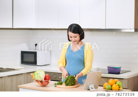 Pregnant woman cutting broccoli for fresh green salad, female prepares tasty organic dinner at home Pregnant woman cutting broccoli for fresh green salad, female prepares tasty organic dinner at home 78273539