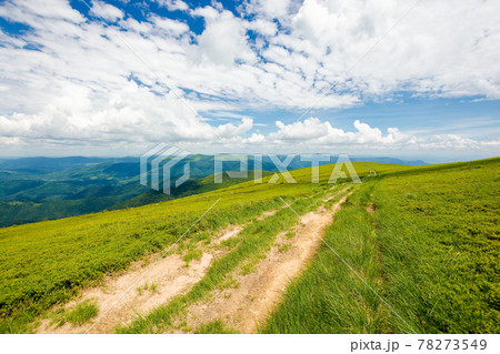 wide trail through grassy meadow. mountain ridge in the distance beneath a gorgeous cloudscape on the blue sky. travel backcountry concept 78273549
