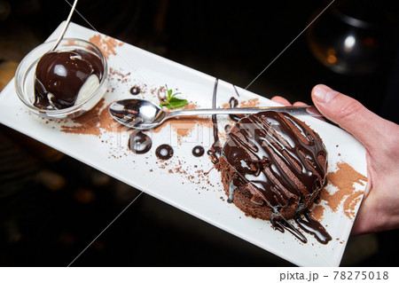The waiter holds in his hand a classic chocolate fondant with ice cream. Close-up, selective focus The waiter holds in his hand a classic chocolate fondant with ice cream. Close-up, selective focus 78275018