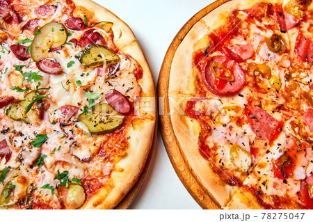Pizza with salami, bell pepper, tomatoes and cheese, pickles, bacon and sausages on a light background. Close-up, selective focus Pizza with salami, bell pepper, tomatoes and cheese, pickles, bacon and sausages on a light background. Close-up, selective focus 78275047