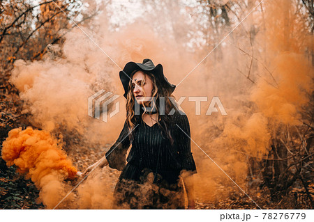 Girl dressed as witch holding smoke bomb in her hands on forest background Girl dressed as witch holding smoke bomb in her hands on forest background 78276779
