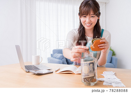 家計簿をつけながら小銭を小瓶に貯める女性 78288088