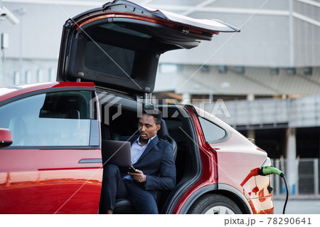 African man working on laptop while electric car is charging African man working on laptop while electric car is charging 78290641