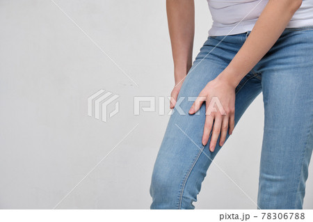 A girl in a white T-shirt and jeans is massaging her thigh. It drives the muscle. A girl in a white T-shirt and jeans is massaging her thigh. It drives the muscle. 78306788