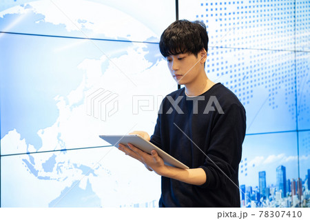 大型ディスプレイの前でタブレットを見る若い男性 大型ディスプレイの前でタブレットを見る若い男性 78307410