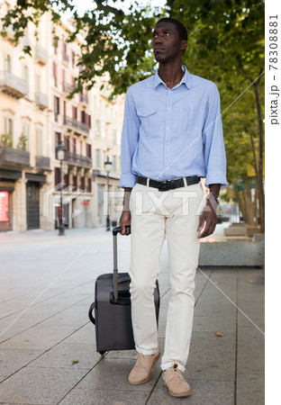 African american traveler strolling with luggage along city street African american traveler strolling with luggage along city street 78308881