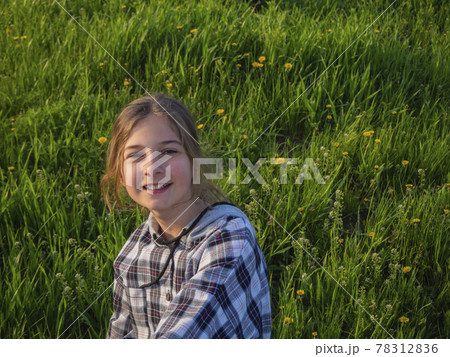 Smiling teenage girl on a walk in the park sits on a blooming green meadow in the sun. 78312836
