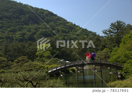 日本庭園の橋の上で傘をさしながら景色を見る夫婦 78317691