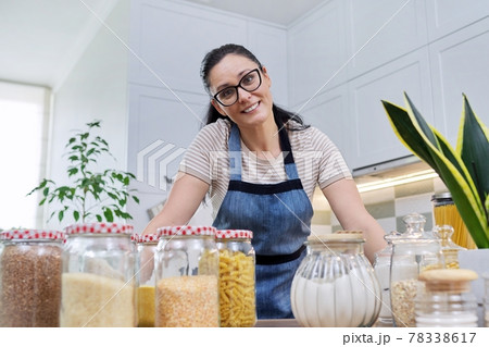 Storing food in kitchen, woman with jars and containers talking and looking at camera Storing food in kitchen, woman with jars and containers talking and looking at camera 78338617
