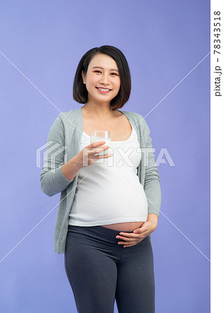 Young pregnant woman with glass of milk over purple background 78343518