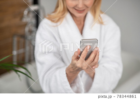 A woman in a white bath robe with a smartphone in her hands A woman in a white bath robe with a smartphone in her hands 78344861