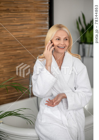 A woman in a white bath robe with a smartphone in her hands 78344863