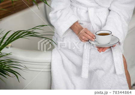 Woman in a white robe holding a cup with tea Woman in a white robe holding a cup with tea 78344864