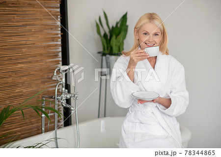 Woman in a white robe holding a cup with tea Woman in a white robe holding a cup with tea 78344865