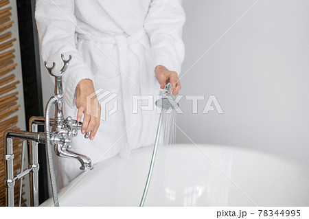 Close up of a woman in a white bath robe holding the shower 78344995