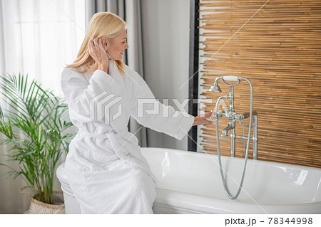 Blonde pretty woman in a white bath robe getting the bath ready 78344998