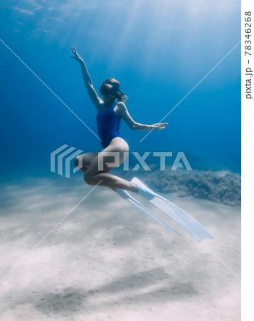 Lady freediver with fins posing and glides underwater in ocean with sunlight. Freediving in warm water 78346268