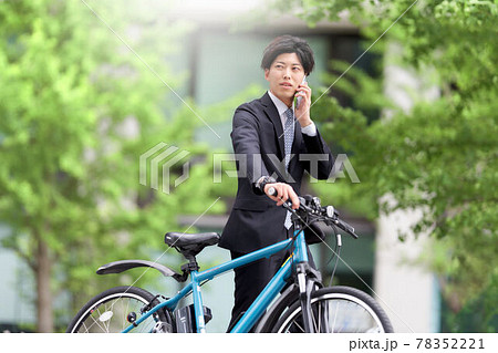 自転車を押しながらスマホで通話する若い男性 78352221